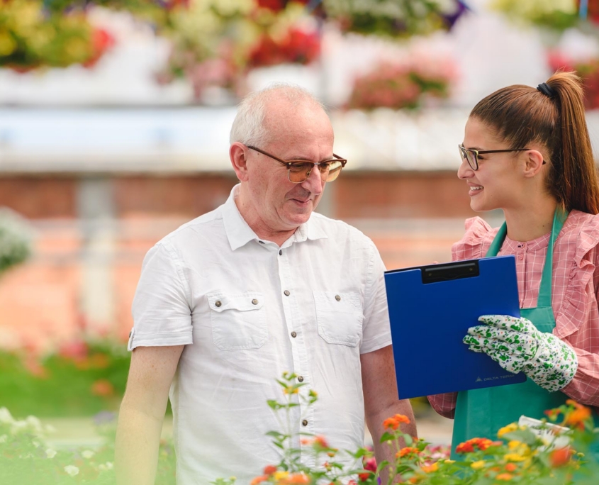 Man And Woman In Greenhouse Looking Flowers